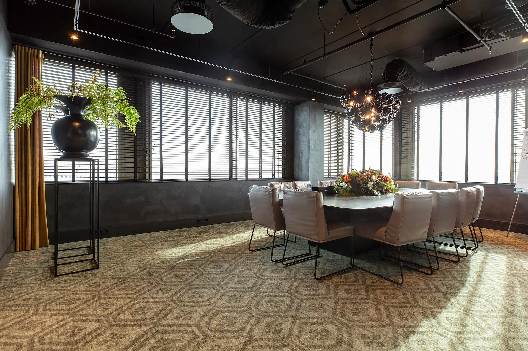 Vergaderruimte aan de Vliegend Hertlaan met een grote ovale tafel, moderne stoelen, sierverlichting en bloemstuk als middelpunt.